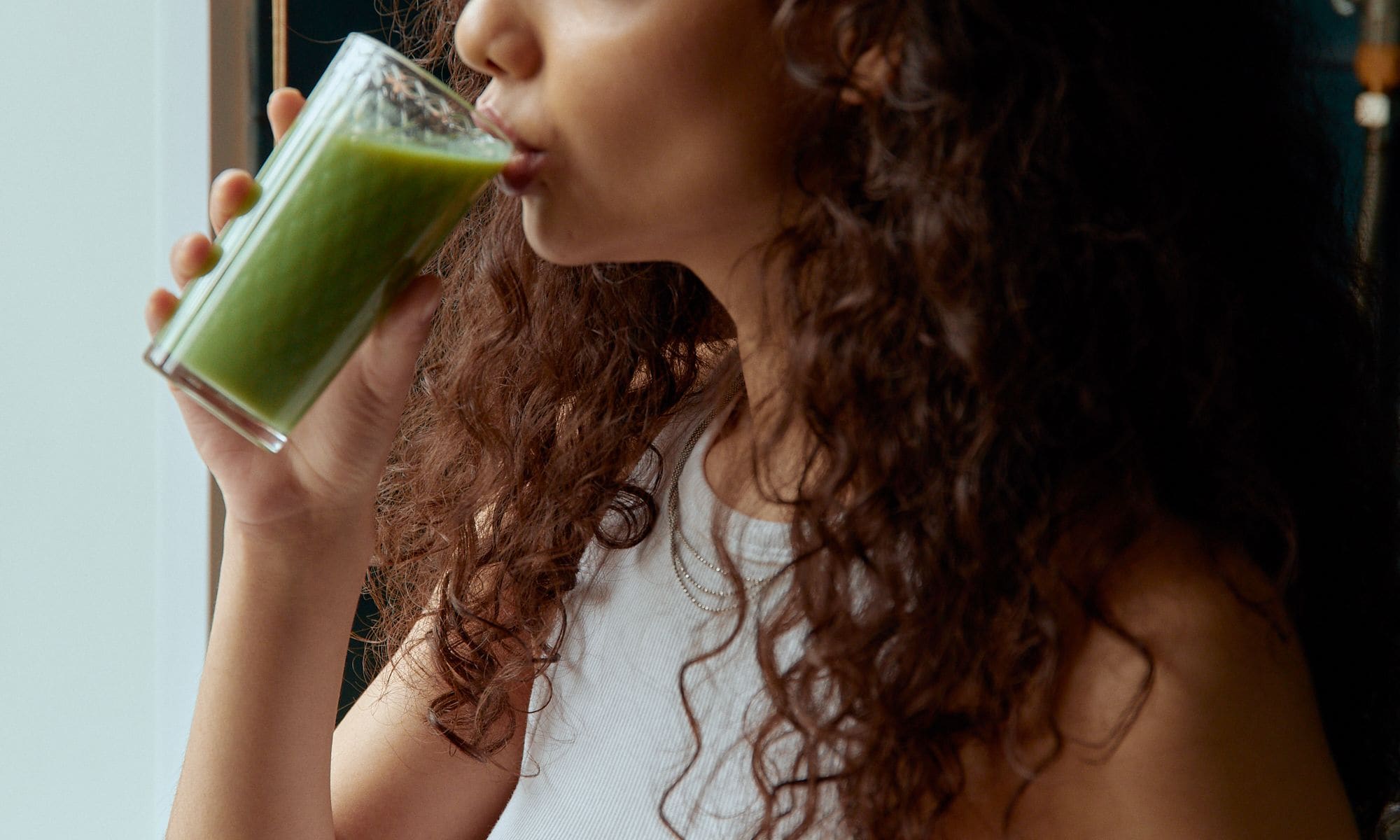 Persona tomando un batido verde junto a la ventana